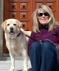 A blonde woman sitting with a white lab dog on a leash