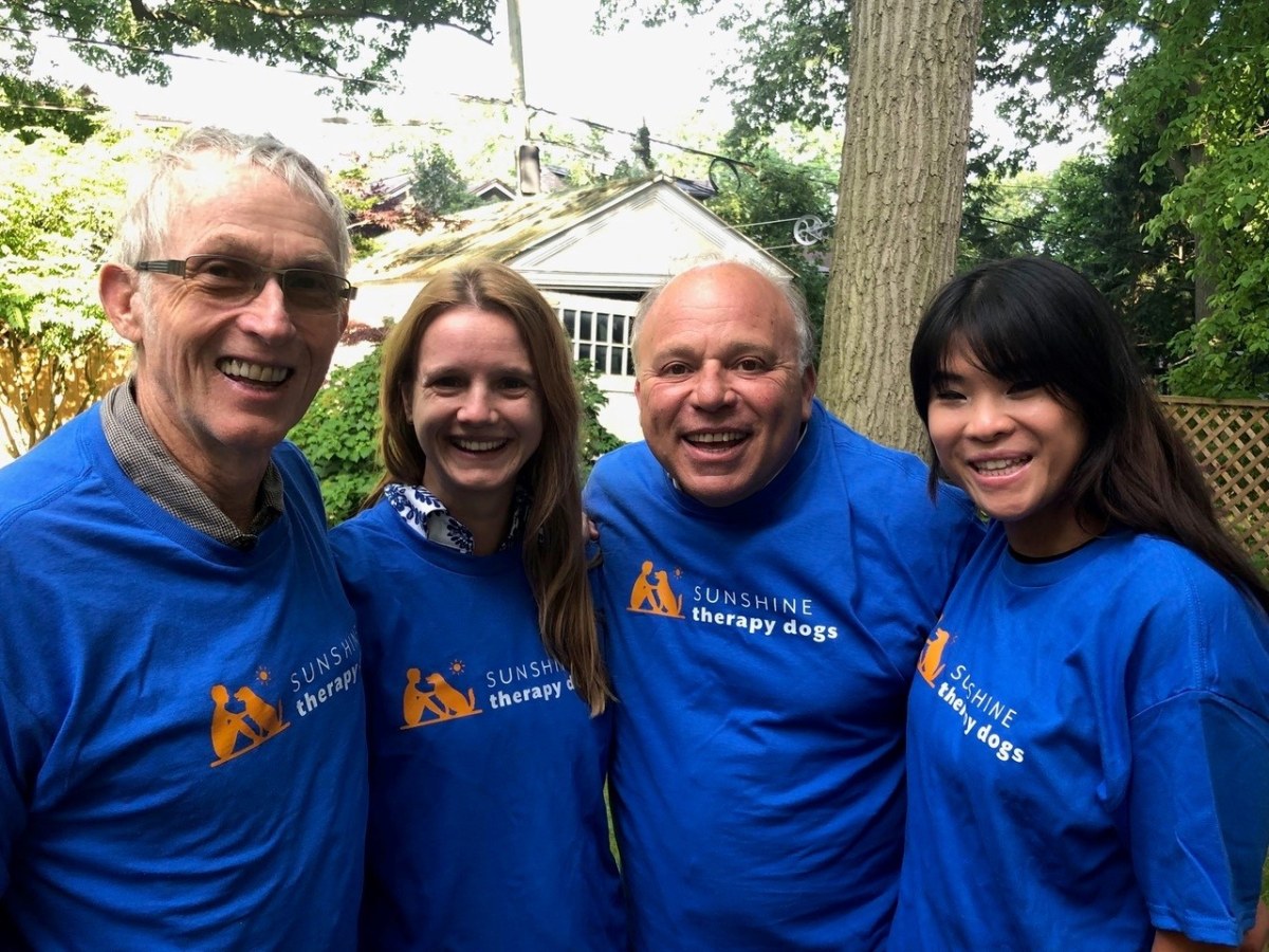 Two men and two women pose outside wearing blue t-shirts with Sunshine Dog Therapy logos on the front.